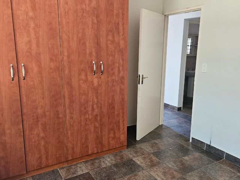 A bedroom featuring built-in wooden wardrobes, tiled flooring, and an open doorway leading to an adjacent room.