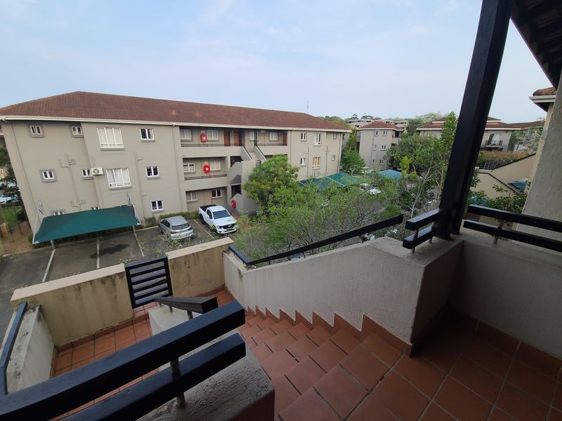 An elevated outdoor staircase and balcony area overlooking the apartment complex parking and grounds, featuring tiled steps and metal safety railings.