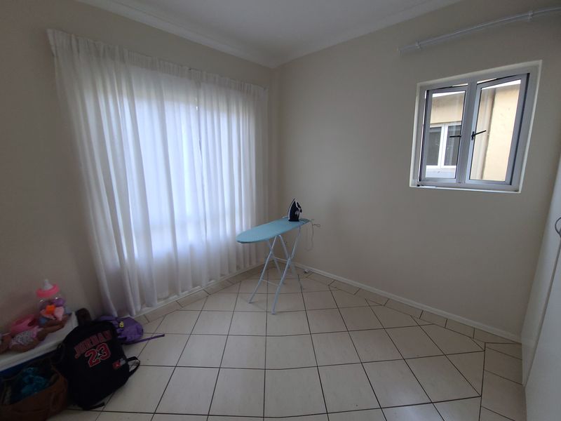 A neutral, empty bedroom featuring tiled flooring, a built-in cupboard, and natural light through a window and curtained glass door.