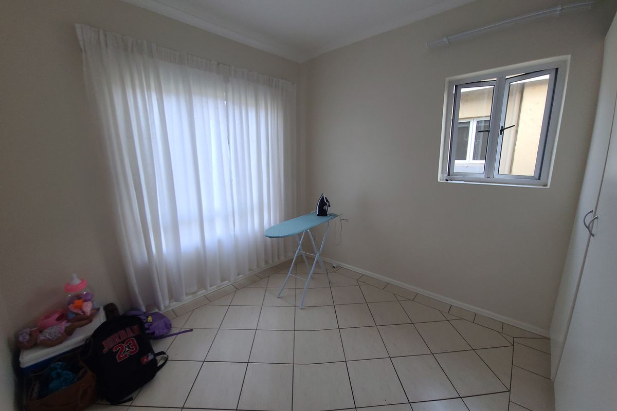 A neutral, empty bedroom featuring tiled flooring, a built-in cupboard, and natural light through a window and curtained glass door.