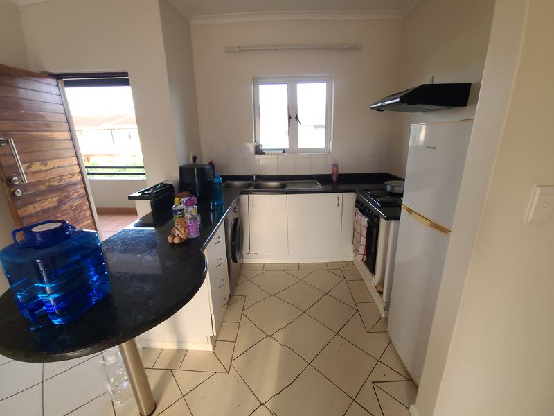 Compact kitchen featuring granite countertops, built-in cabinetry, integrated oven and hob, and tiled flooring with direct access to an outdoor balcony area.