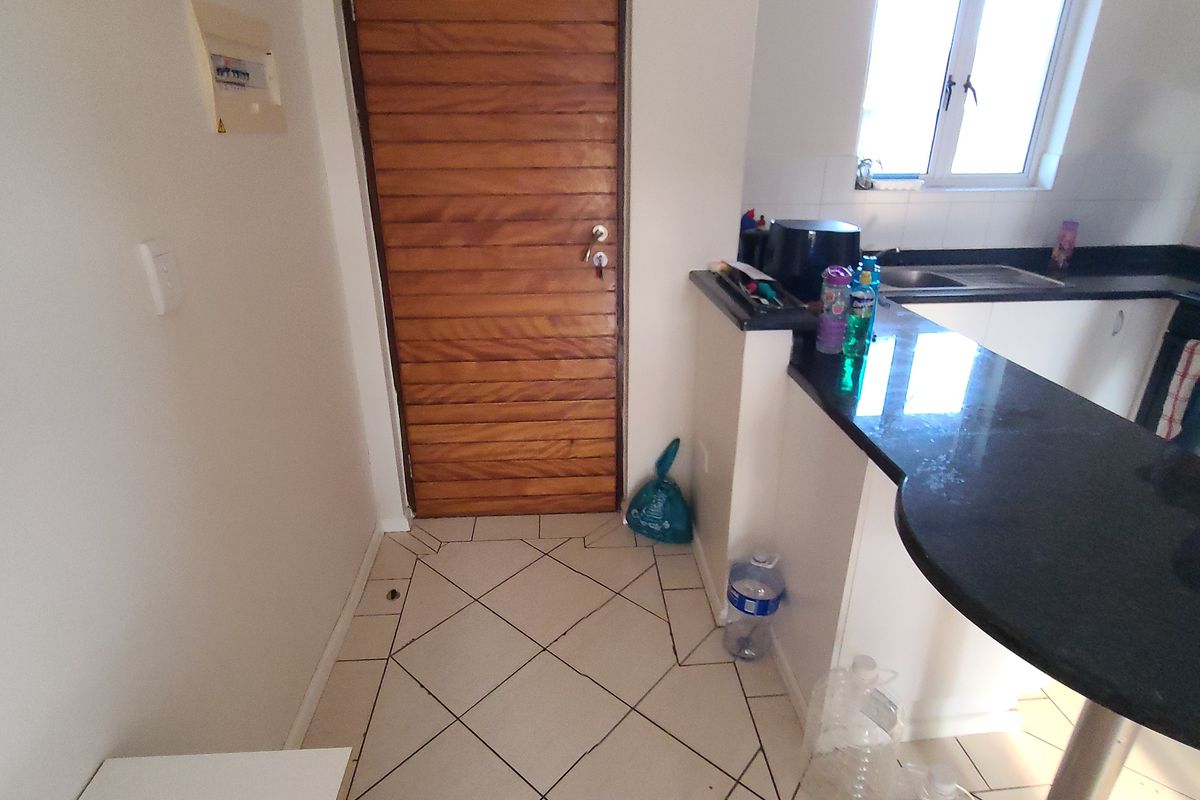 A functional kitchen area featuring dark granite countertops, tiled flooring, and a wooden door, providing a practical layout for daily use.