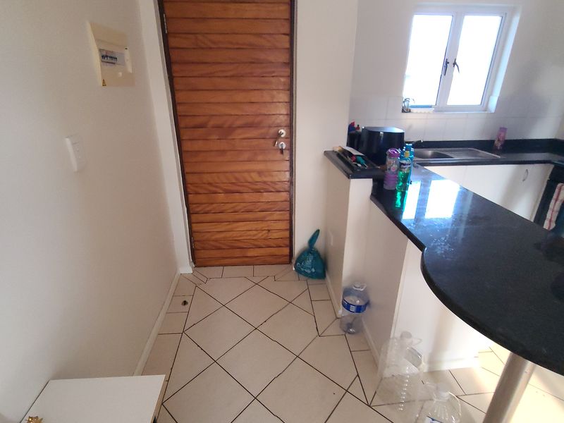 A functional kitchen area featuring dark granite countertops, tiled flooring, and a wooden door, providing a practical layout for daily use.