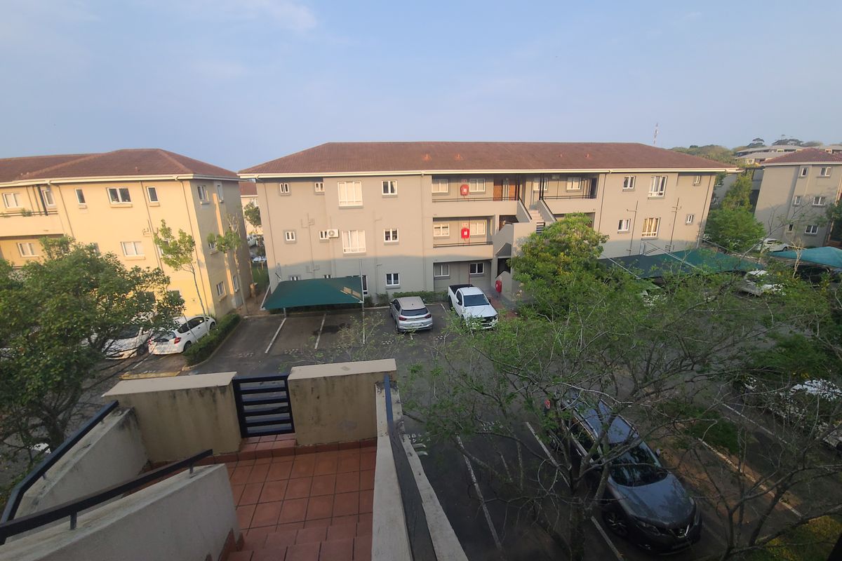 Elevated view of an apartment complex exterior featuring a tiled stairwell, parking area with shade cloth carports, and multi-story residential buildings.