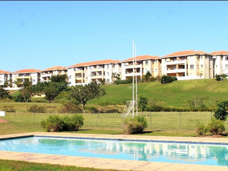 A well-maintained communal swimming pool area set within landscaped grounds, featuring paved surrounds and views of the apartment complex.