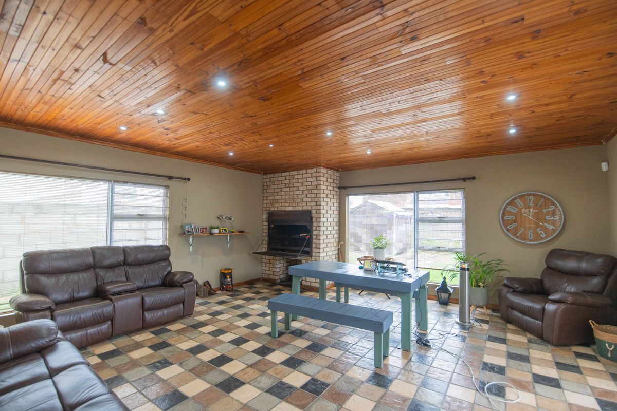 Spacious living area featuring a timber-clad ceiling, tiled flooring, and a built-in brick fireplace with access to the rear garden.