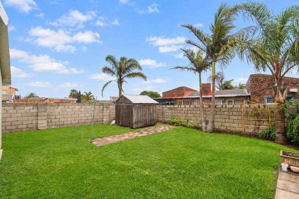 A private rear garden featuring a lawn, paved walkway, and a wooden storage shed enclosed by concrete block boundary walls.