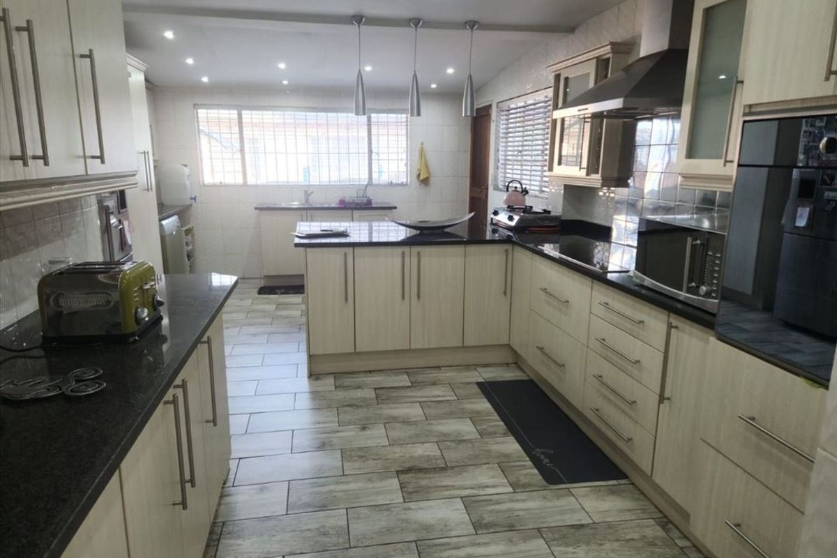 Spacious kitchen featuring light wood cabinetry, dark granite countertops, built-in oven, extractor fan, and modern tiled flooring with ample workspace.