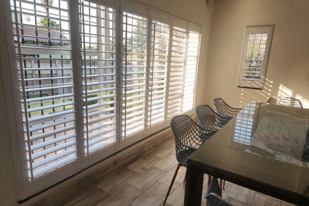 A bright, enclosed patio area featuring wood-look tile flooring and extensive white plantation shutters, providing a seamless transition to the outdoor space.