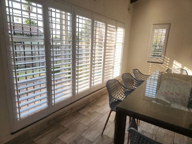 A bright, enclosed patio area featuring wood-look tile flooring and extensive white plantation shutters, providing a seamless transition to the outdoor space.