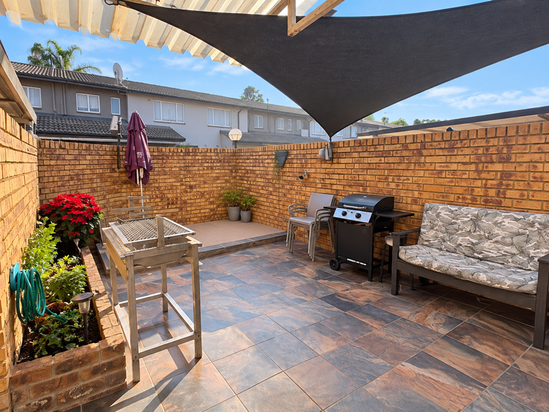 A private outdoor patio area featuring tiled flooring, brick boundary walls, a raised planter box, and a shade sail for sun protection.