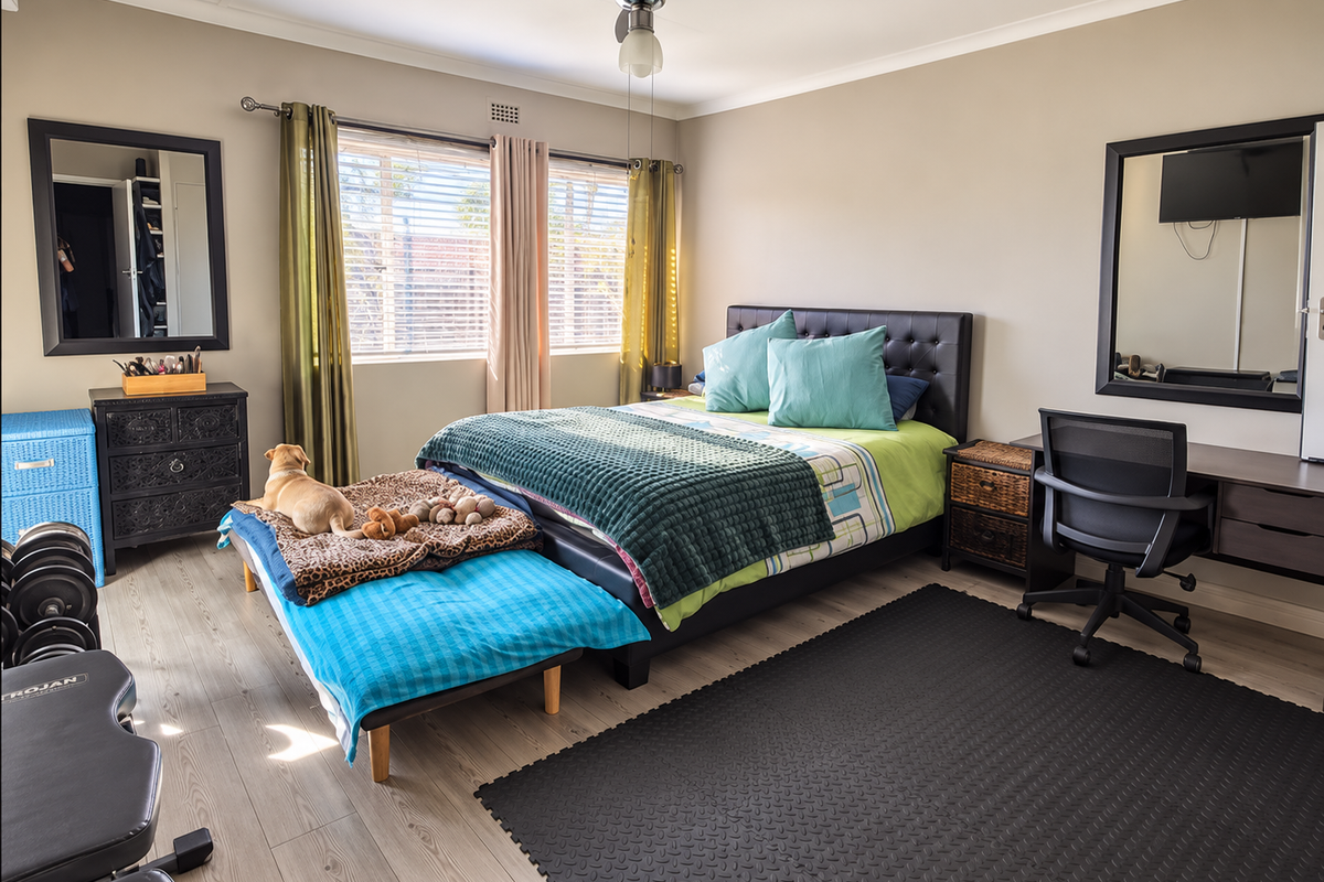 A well-maintained bedroom featuring laminate flooring, a ceiling fan, and a built-in desk area with large wall-mounted mirrors.