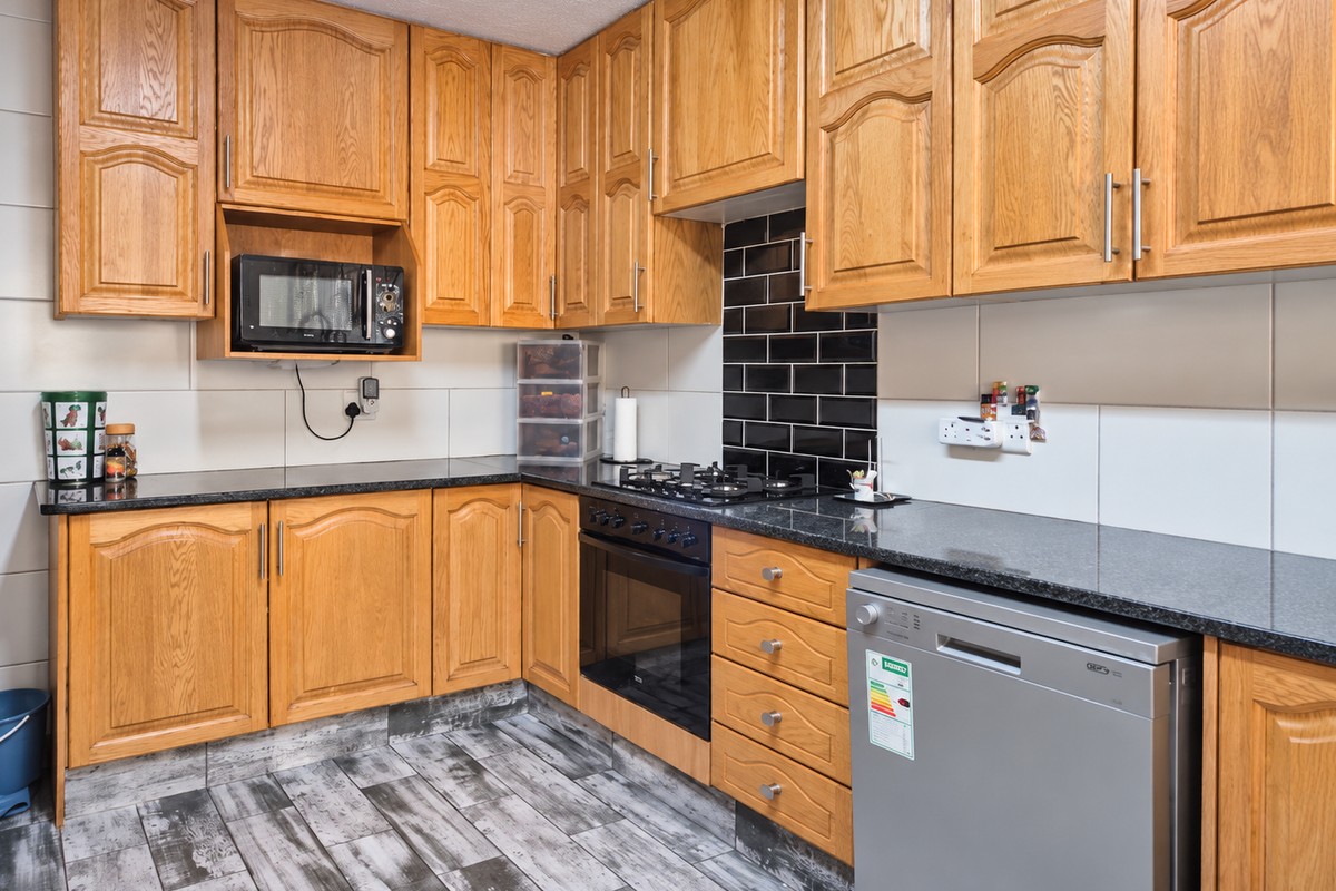A functional kitchen featuring traditional oak cabinetry, granite countertops, a black subway tile backsplash, and built-in cooking appliances.