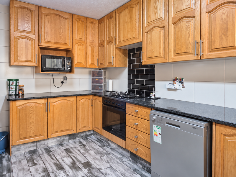 A functional kitchen featuring traditional oak cabinetry, granite countertops, a black subway tile backsplash, and built-in cooking appliances.