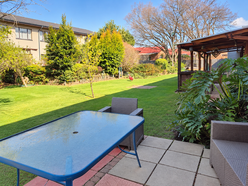 A spacious rear garden featuring a paved patio area, a timber pergola, and a well-maintained lawn, providing an ideal space for outdoor relaxation.