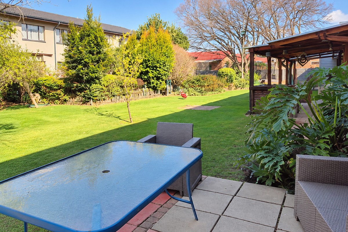 A spacious rear garden featuring a paved patio area, a timber pergola, and a well-maintained lawn, providing an ideal space for outdoor relaxation.