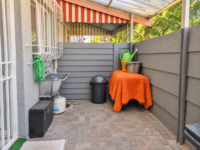 A functional outdoor patio area featuring a stainless steel utility sink, paved flooring, and a protective awning, providing a practical space for utility tasks.