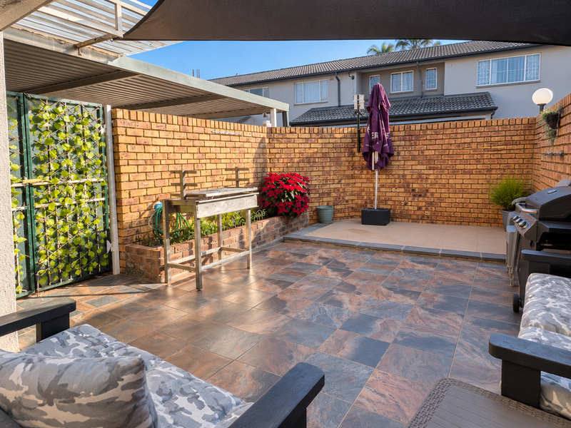A private outdoor patio area featuring tiled flooring, a brick boundary wall, and a metal pergola structure, ideal for outdoor entertaining.