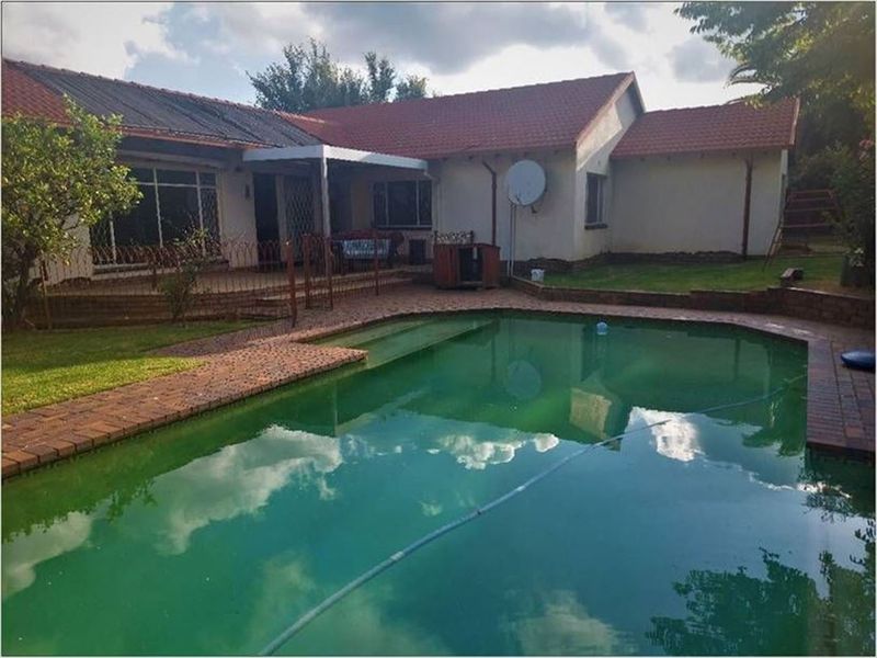 Rear exterior view featuring a swimming pool with brick paving, a covered patio area, and a tiled roof house structure.