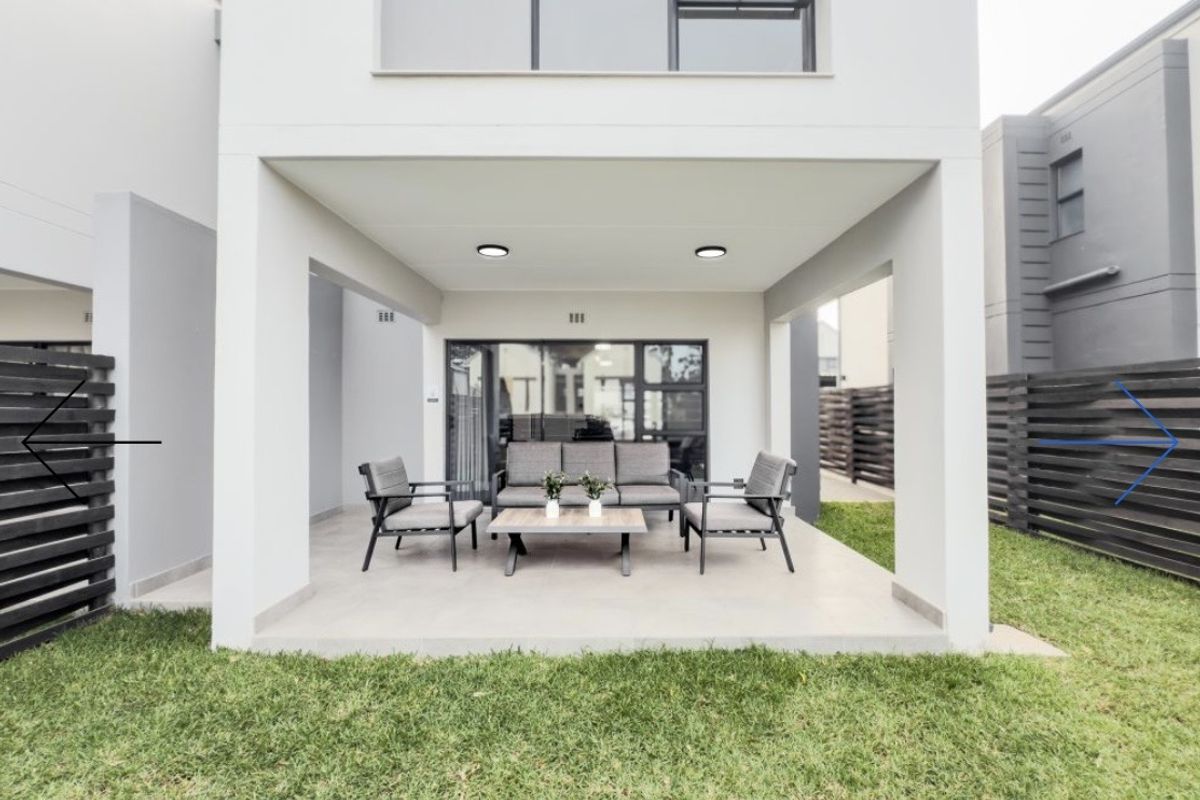 A modern covered patio area featuring tiled flooring and recessed lighting, providing seamless access to the rear garden through large sliding glass doors.