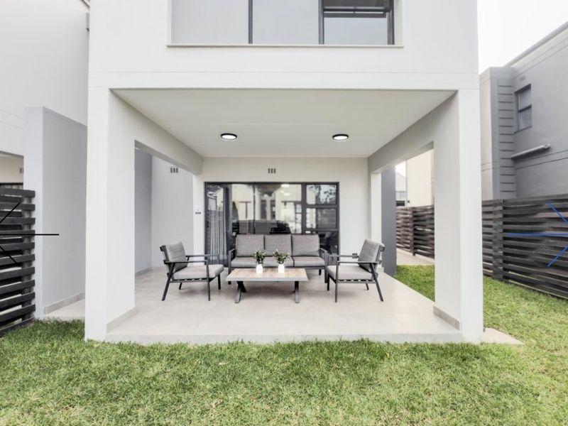 A modern covered patio area featuring tiled flooring and recessed lighting, providing seamless access to the rear garden through large sliding glass doors.