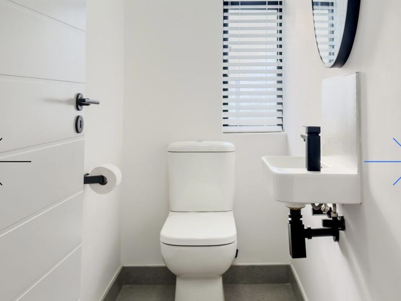 A modern, minimalist guest bathroom featuring a wall-mounted basin, toilet, and sleek black fixtures with clean white finishes.