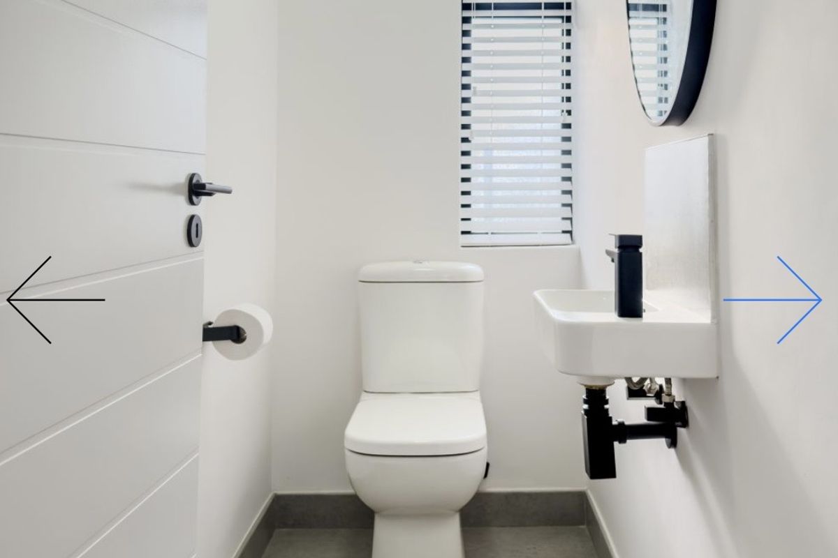 A modern, minimalist guest bathroom featuring a wall-mounted basin, toilet, and sleek black fixtures with clean white finishes.