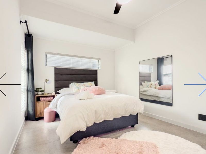 A bright and well-maintained bedroom featuring tiled flooring, a ceiling fan, and a large wall-mounted mirror, offering a clean and functional living space.