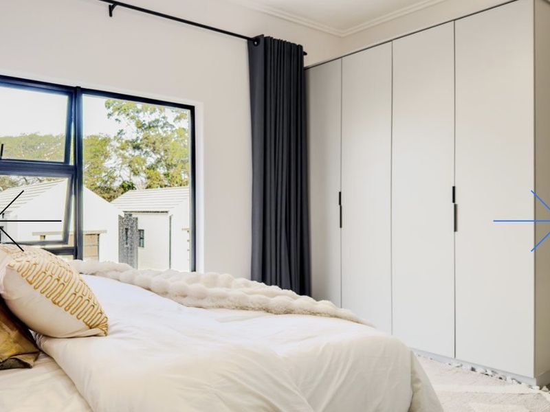 A modern bedroom featuring sleek built-in wardrobes, large aluminium-framed windows, and clean finishes, offering a bright and contemporary living space.