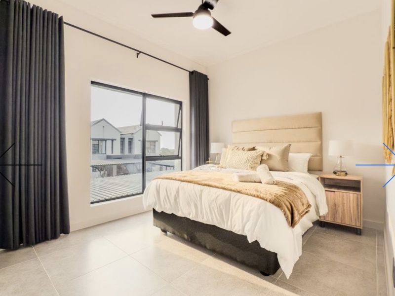 A well-maintained bedroom featuring neutral tiled flooring, modern aluminium window frames, and a ceiling fan.