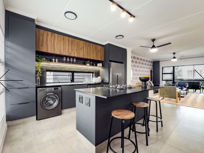 Modern open-plan kitchen featuring a central island with gas cooktop, sleek dark cabinetry, integrated laundry appliance, and contemporary track lighting.