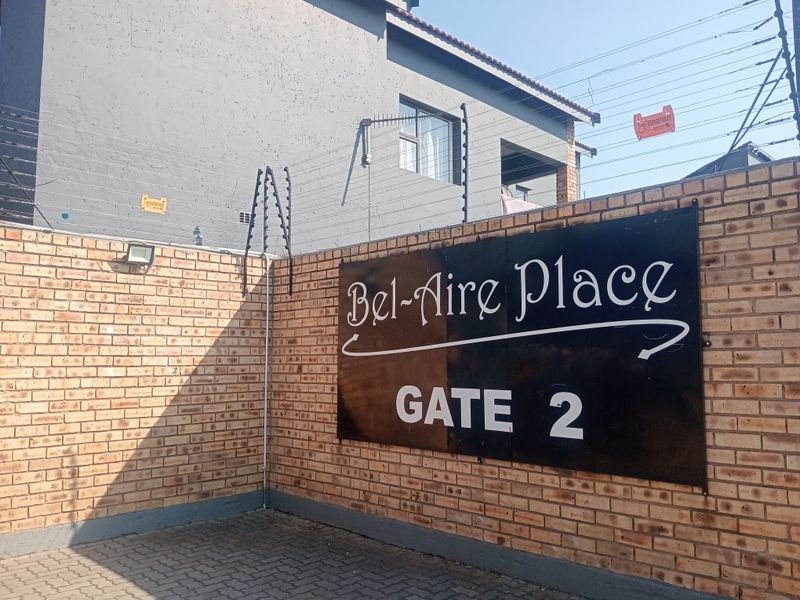 Entrance view of Bel-Aire Place Gate 2, featuring a brick boundary wall with integrated electric security fencing and paved driveway access.