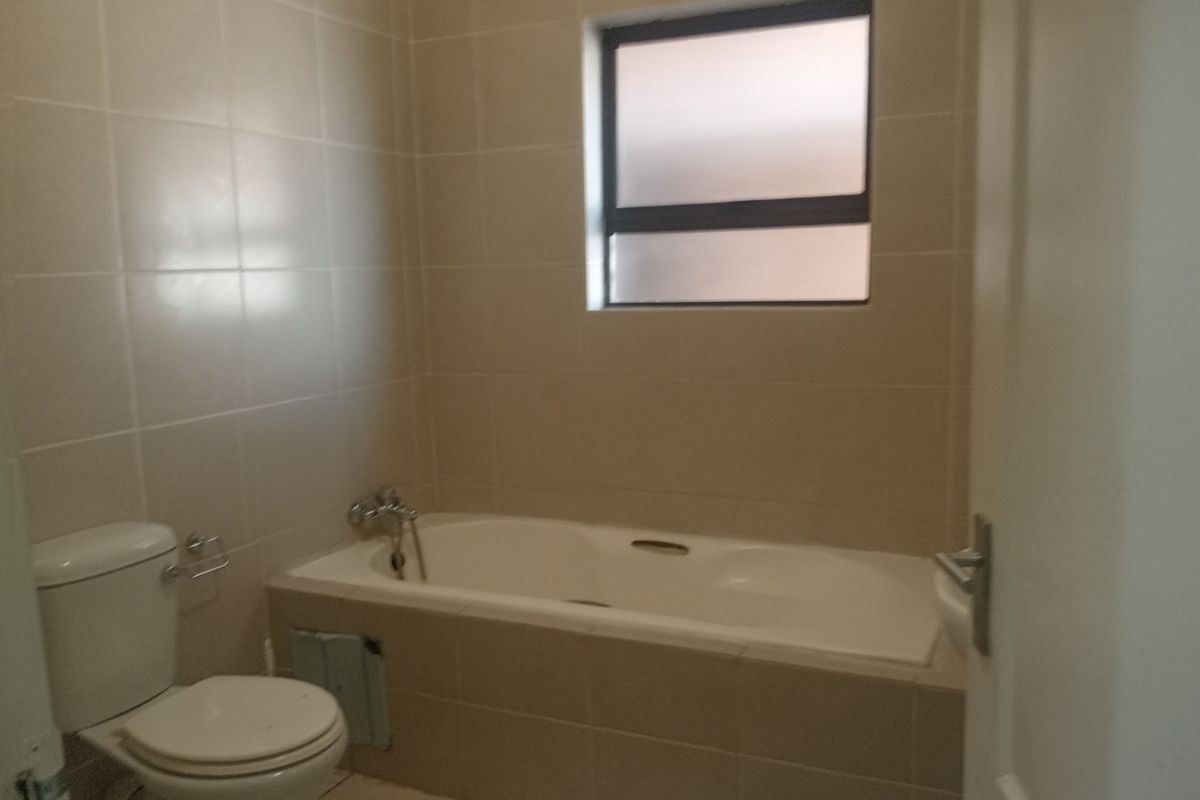 A functional bathroom featuring a bathtub, toilet, and neutral wall tiling. The space requires a bath panel replacement to complete the finish.