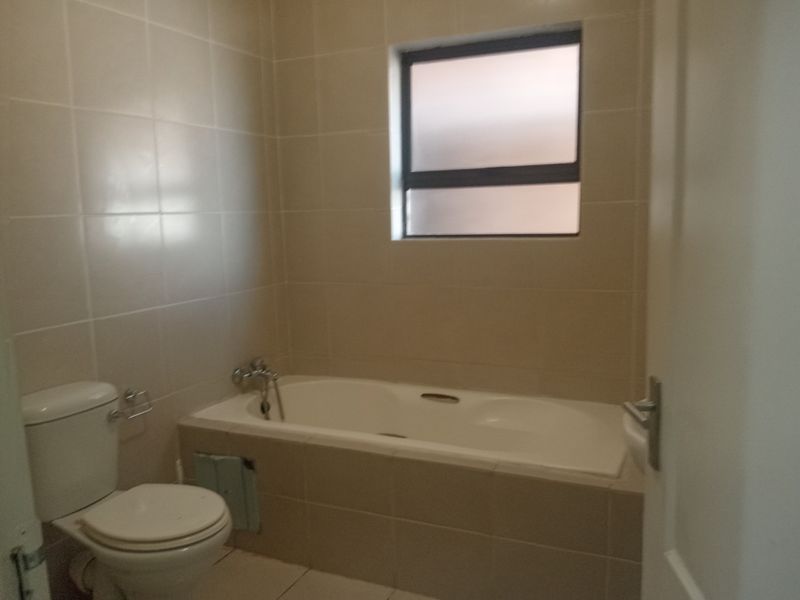 A functional bathroom featuring a bathtub, toilet, and neutral wall tiling. The space requires a bath panel replacement to complete the finish.