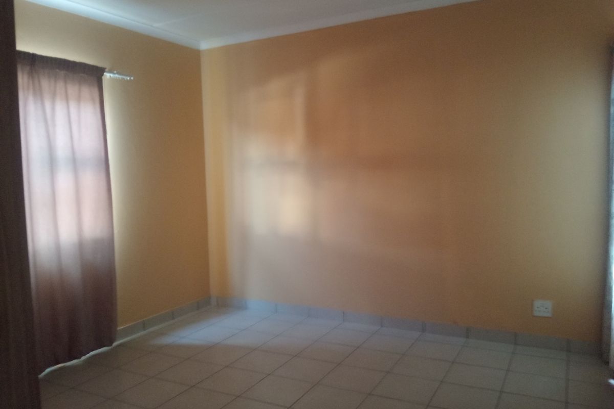 A vacant bedroom featuring neutral tiled flooring, painted walls, and a window with installed curtain tracks.