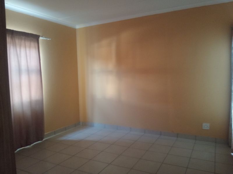 A vacant bedroom featuring neutral tiled flooring, painted walls, and a window with installed curtain tracks.