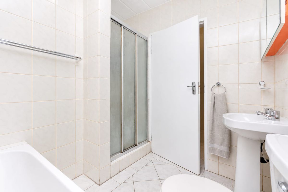 A functional bathroom featuring a pedestal basin, bathtub, and a separate shower enclosure with tiled walls and flooring throughout.