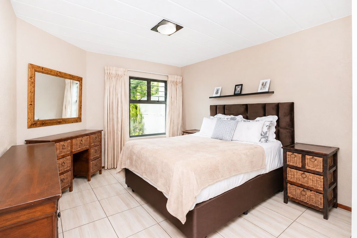 A well-lit bedroom featuring neutral wall tones, tiled flooring, and a window with security bars.