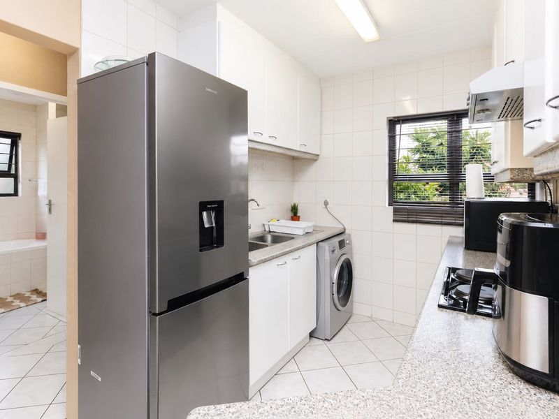 A functional kitchen featuring white cabinetry, granite countertops, a gas hob with extractor fan, and tiled finishes, with an adjacent bathroom visible.