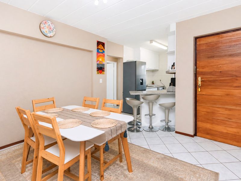 Open plan dining area flowing into a functional kitchen with a breakfast bar and tiled flooring.