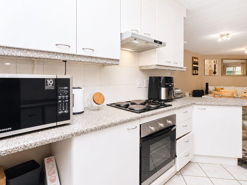 Open-plan kitchen featuring white cabinetry, granite countertops, built-in oven, gas hob, and extractor fan, flowing into the adjacent living area.