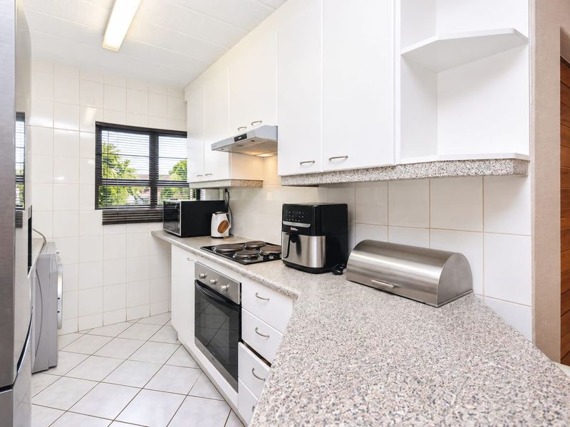 A functional kitchen featuring white cabinetry, granite countertops, built-in oven and hob, and tiled finishes throughout.
