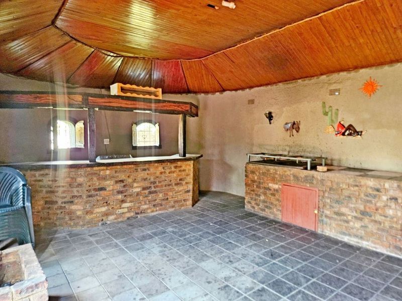 Rustic entertainment area featuring a built-in brick bar, integrated braai, tiled flooring, and a distinctive timber-clad vaulted ceiling.