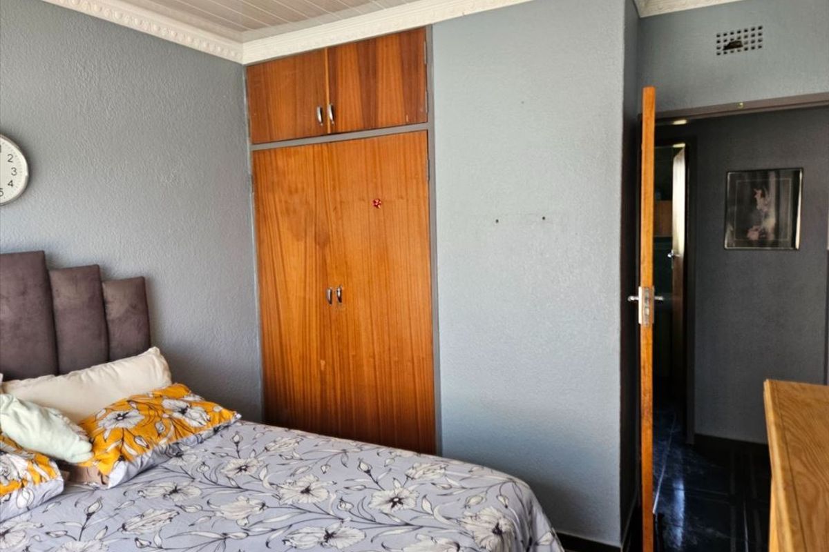 A bedroom featuring built-in wooden cupboards, decorative ceiling cornices, and tiled flooring, offering a functional space with potential for modern updates.