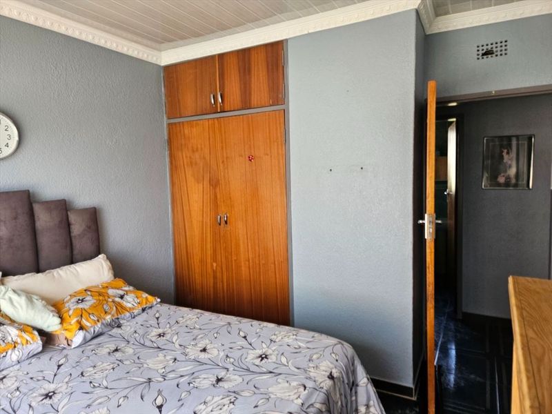 A bedroom featuring built-in wooden cupboards, decorative ceiling cornices, and tiled flooring, offering a functional space with potential for modern updates.