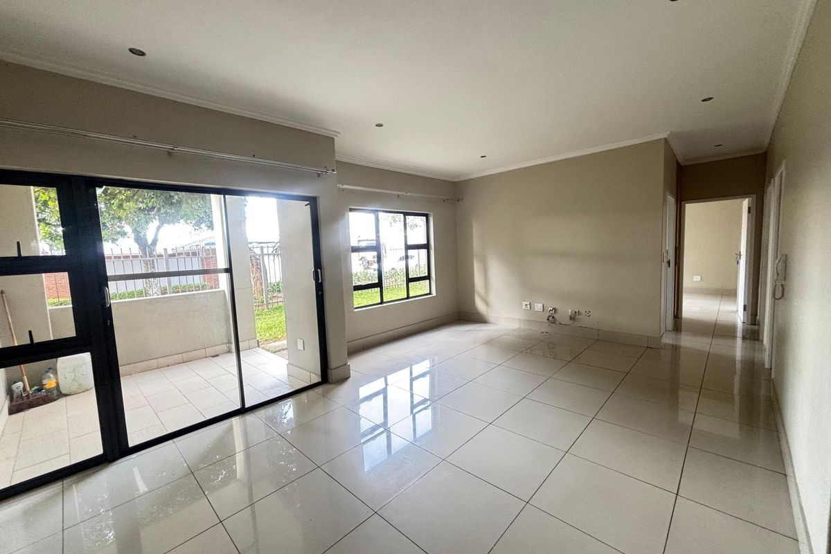 A bright, empty living room featuring polished porcelain floor tiles, recessed downlighting, and large sliding glass doors leading to an outdoor patio area.