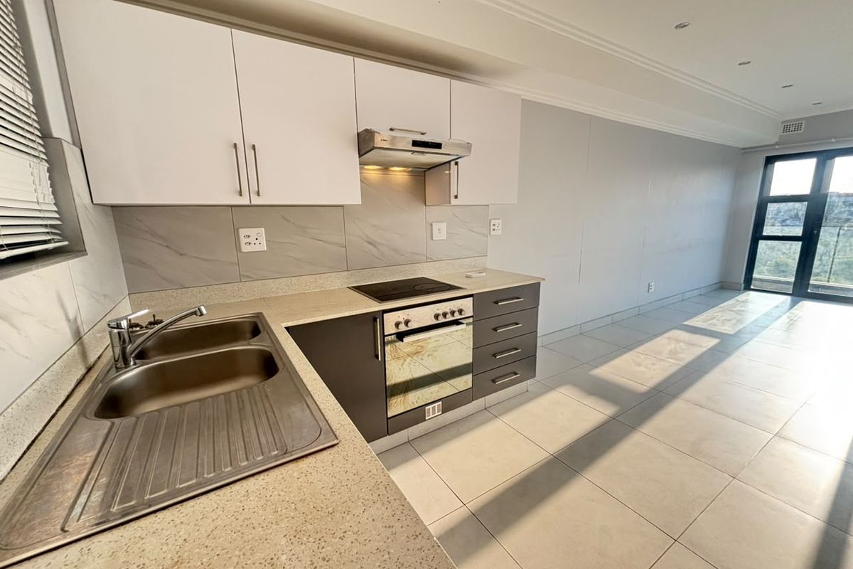 Modern open-plan kitchen featuring sleek cabinetry, stone countertops, integrated appliances, and tiled flooring, flowing into a bright living area with balcony access.