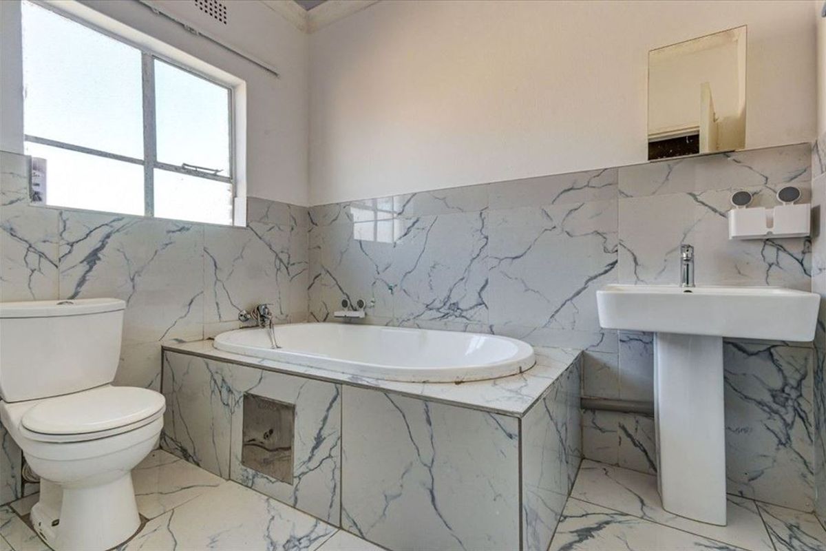 A functional bathroom featuring marble-effect wall and floor tiling, a pedestal basin, and a built-in bathtub with chrome fixtures.