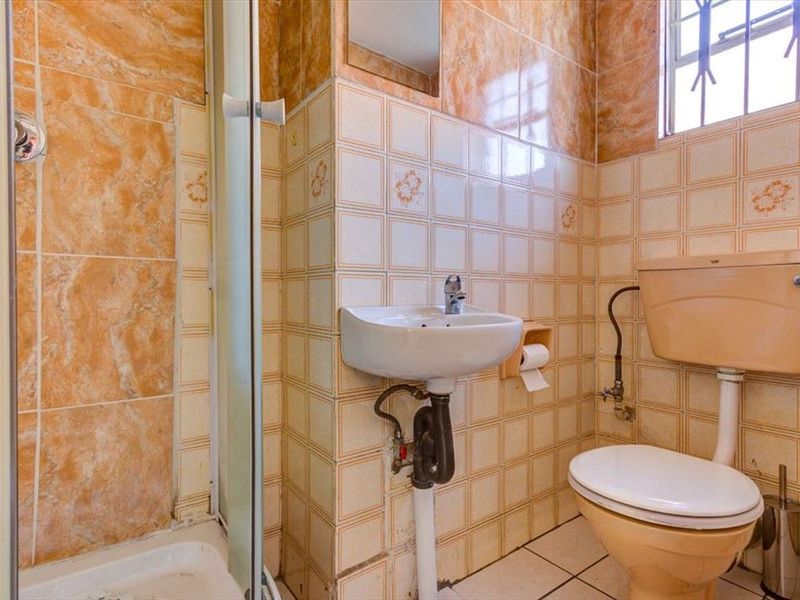 A compact bathroom featuring a shower enclosure, wall-mounted basin, and toilet, finished with dated ceramic wall and floor tiles.