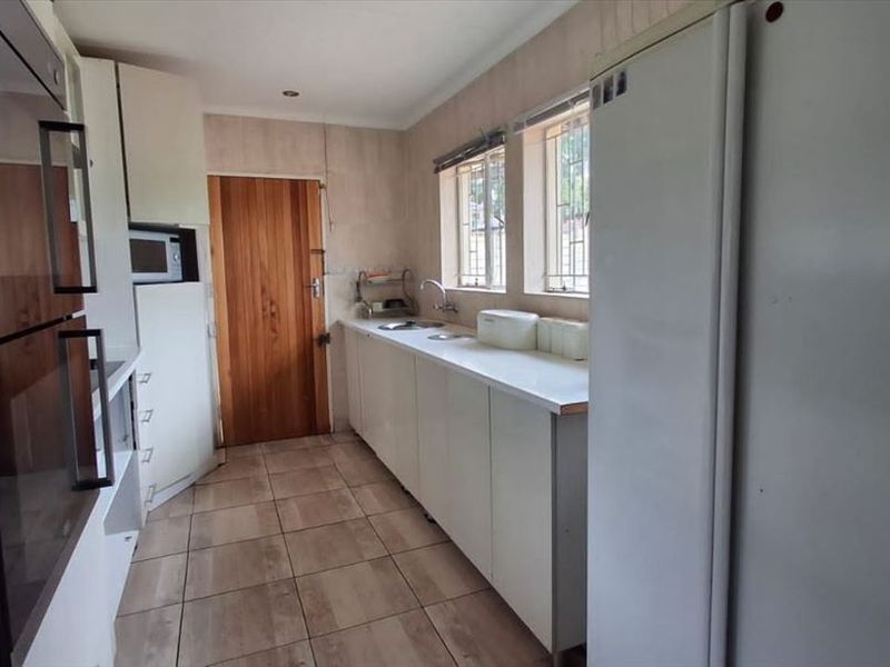 A functional kitchen featuring built-in appliances, laminate countertops, a double sink, and tiled flooring with security bars on the windows.